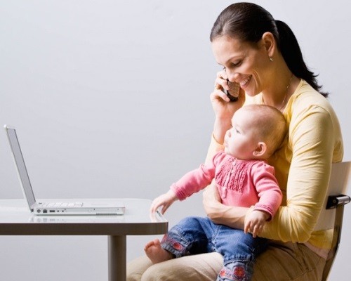 Working mother holding baby while talking on cell phone at desk