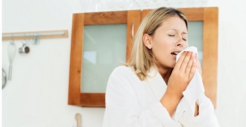 young woman in a bathrobe sneezing into a tissue