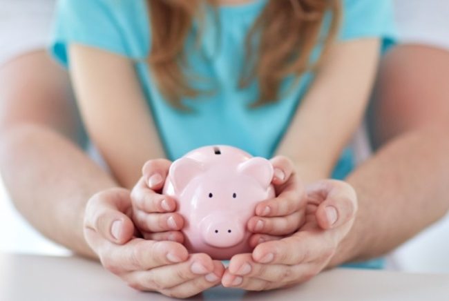 close up of family hands with piggy bank